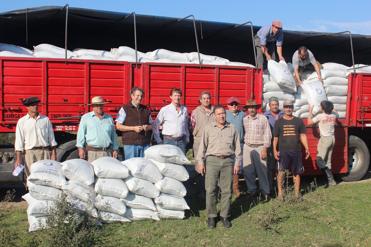 Group of farmers loading sacks onto a red truck in the countryside.